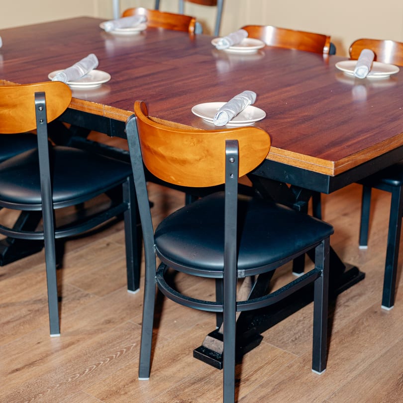 A long wooden dining table with black chairs, set with white plates and rolled napkins.