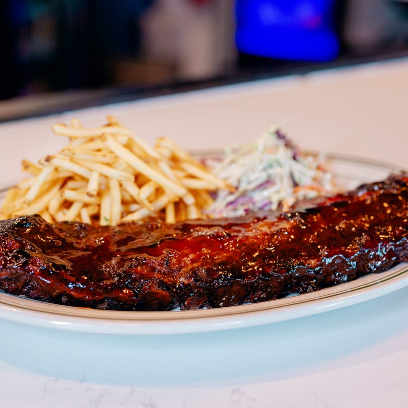 A plate of 83 Tavern's BBQ ribs, french fries, and coleslaw.