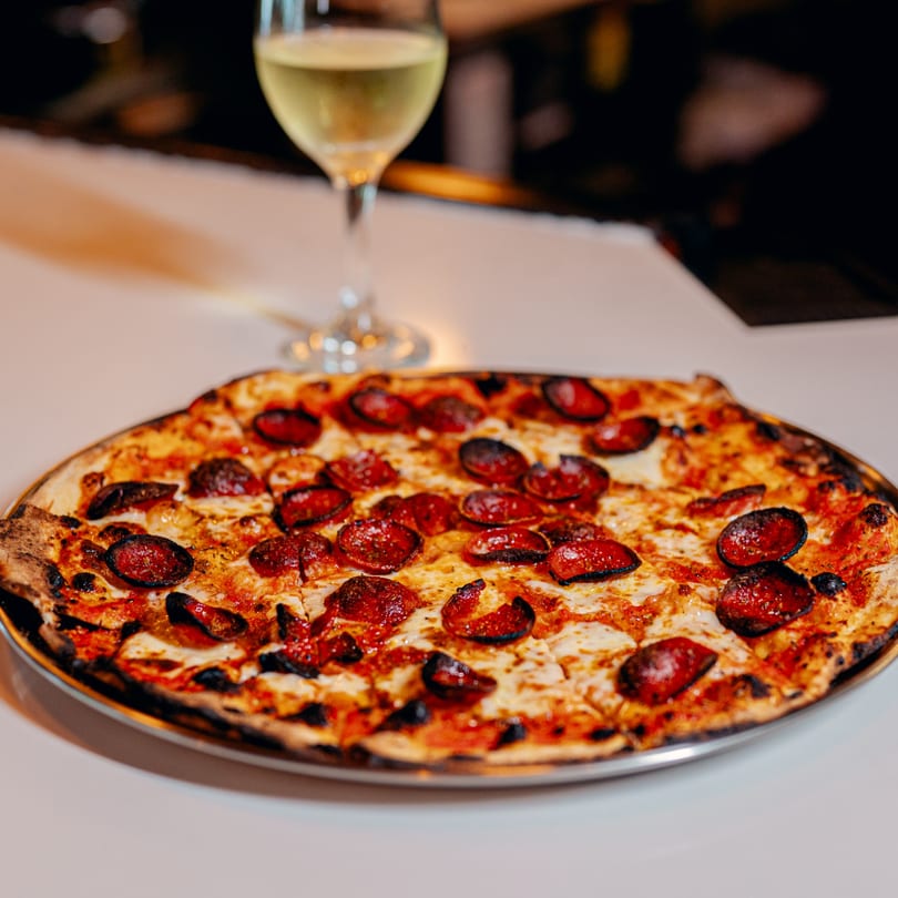 A pepperoni pizza with a crispy crust and melted cheese, alongside a glass of white wine.