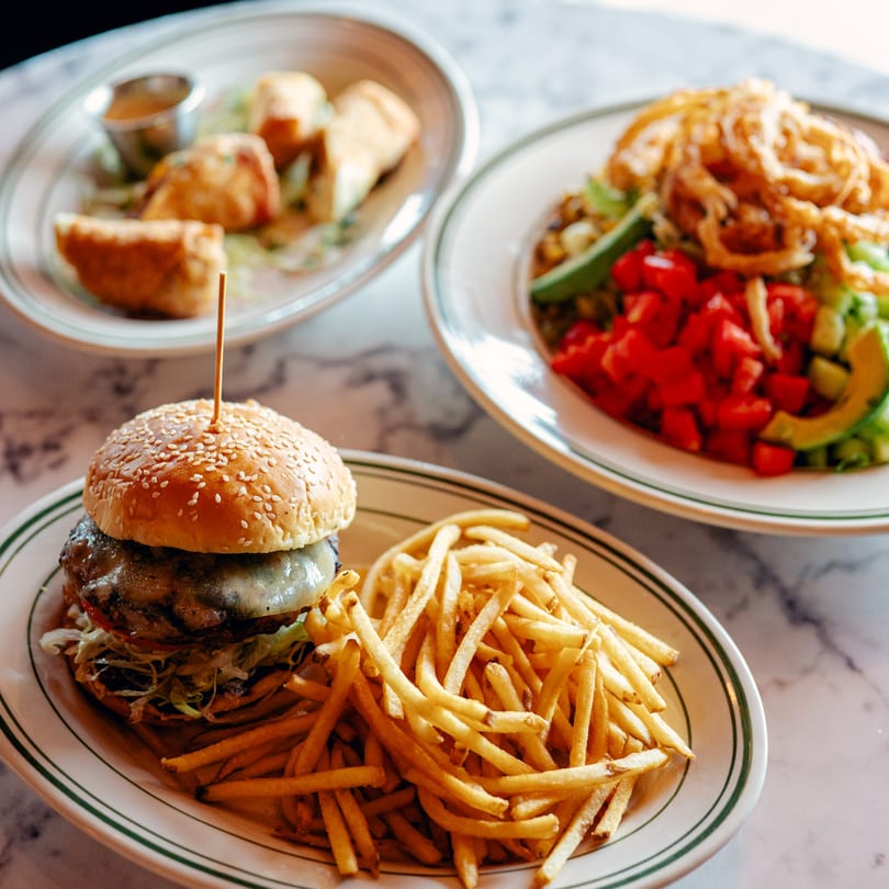 A cheeseburger with fries, a salad, and appetizers on a marble table at 83 Tavern.