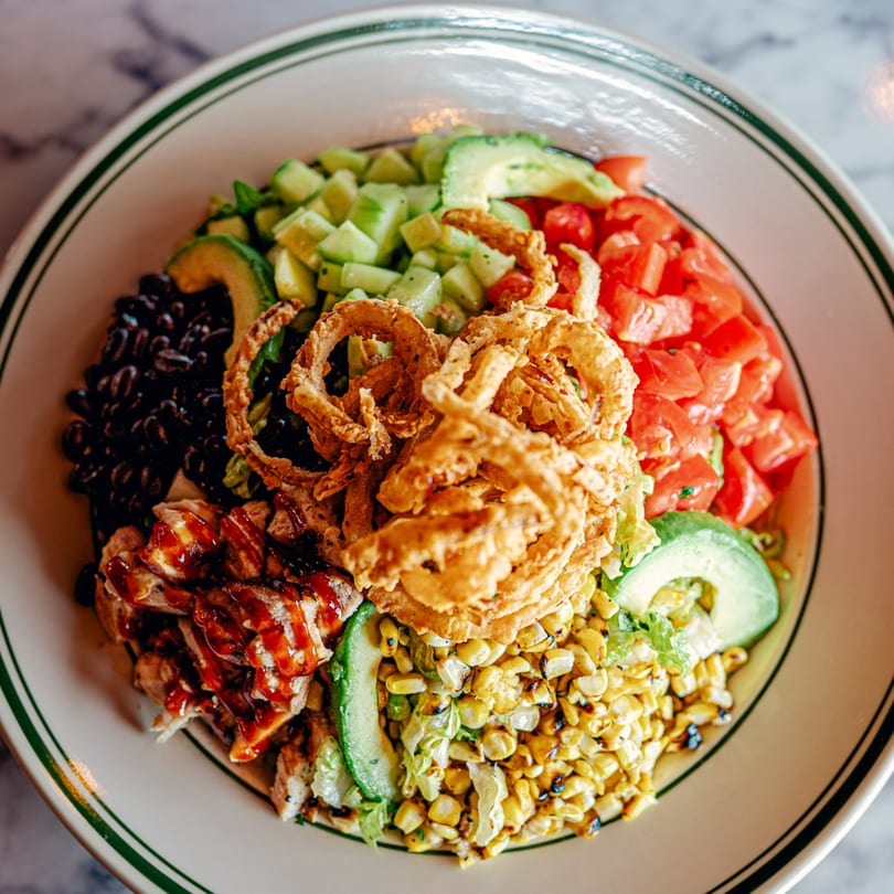 Overhead view of a colorful salad with chicken, black beans, corn, tomatoes, avocado, and onion rings.